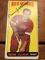 Front of 1964-65 Topps Tall Boy hockey card showing Norm Ullman in Red Wings uniform with autograph in black Sharpie across image.