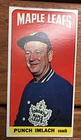 Front photo of the 1964-65 Topps Tall Boy hockey card featuring Punch Imlach with red background and Toronto Maple Leafs blue jacket.