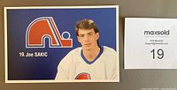 Close-up image of Joe Sakic postcard showing his portrait, team logo, name and number.