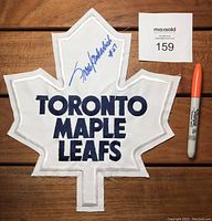 Front view of white fabric Toronto Maple Leafs crest patch with bold blue embroidered text and blue Sharpie autograph of Frank Mahovlich with #27.