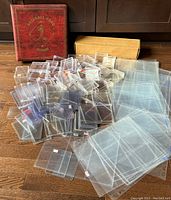 Photo showing a red baseball card album, a cardboard storage box, and a large assortment of clear plastic card holders and sheets.
