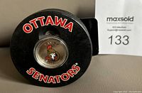 Top of black hockey puck showing Ottawa Senators logo and encapsulated $1 coin