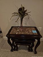 Front view of three wood nesting tables with stone tops stacked inside each other and floral arrangement on top