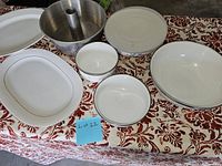 Photo showing an assortment of ceramic bakeware and serving platters on patterned tablecloth including bundt pan, various bowls, and platters.