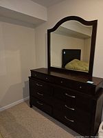 Photo showing dark wood dresser with attached mirror reflecting part of headboard and bed.