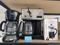 Photo showing Sunbeam coffee maker on left, stainless steel and black Cuisinart coffee maker in middle, and Aroma Cafe Classic coffee press in box on right.