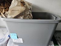 Plastic bin filled with wrapped fall decor items including ceramic pumpkins and artificial leaves.
