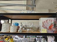 Wide shot of shelf displaying various glass bowls, ceramic jars, figurine, and decorative plate.