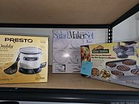 Photo showing all three boxed items: Presto FryDaddy Elite electric deep fryer, Salad Maker Set, and Mini Burger Maker Set.