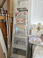 Two aluminum folding step ladders leaning side by side indoors, with paint splatters and signs of use.