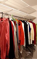 Photo of assorted ladies blouses and tops hanging on a rod, showing coral button-up shirt, various blouses in white, black, red, green, and orange.