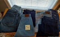 Photo showing folded ladies jeans in various shades of blue denim laid out on a surface with a sticky note showing #129 and sizes 12-14.