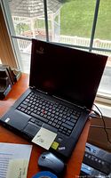 Oblique view of ThinkPad laptop showing screen with Windows Vista logo, keyboard, and black wired mouse on wooden desk