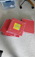 Five red linen photo albums stacked on carpet, each wrapped in plastic with a yellow label on the front cover.