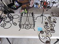 Full view of all four metal home decor pieces arranged on a white table: basket, wine bottle holder, candle holder, and candelabra.