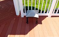 Miniature square metal gazebo with gray fabric top placed on outdoor wooden deck near white railing, shown from top-down angle.