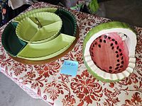 Photo of green ceramic serving platters including a segmented plate with a gold handle and a green oval platter, alongside a watermelon-shaped ceramic basket.