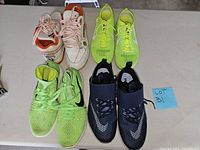 Four pairs of sneakers including neon green Nike shoes, white and orange pair and black and blue pair.
