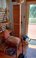 Closed view of one tall louvered door storage cabinet next to window with chair and rack nearby