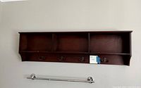 Dark brown wooden wall shelf mounted on wall with three sections and four black metal hooks.