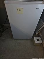 Front view of white mini refrigerator with a post-it note labeled #121 on the door.