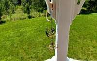 Crescent moon wind chime with turtle and lantern hanging on a white porch column with green lawn background