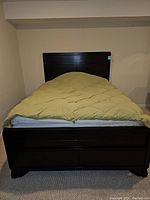 Full view of full size wooden bed frame with mattress and green quilted bedspread.