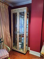 Full view of a tall display cabinet with burled wood veneer finish against a red wall, showing glass doors and contents inside.
