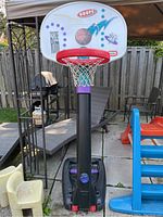 Front view of entire basketball hoop showing backboard, rim, net, black support pole, and black base with red wheels in outdoor setting.
