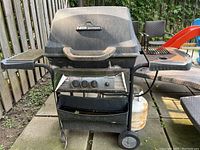 Full view of black Fiesta Dynasty 450 barbecue grill with side shelves and wheels in outdoor setting.