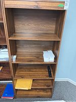 Photo of MDF laminate bookcase showing two fixed and one adjustable shelf with some wear on shelf edges, empty except for some small paper stack contents not included.