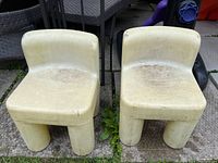 Two weathered off-white plastic children's chairs placed side by side outside on concrete.