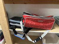 Two soft-sided cooler bags stacked on a wooden shelf, one red with graphic icons and the other gray with black accents, showing side and angled views.