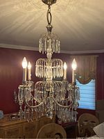 Full view of the chandelier suspended from the ceiling showing six lit bulbs, metal frame, and hanging crystals.