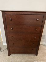 Front view of the 5 drawer wood dresser with minor scratches noted along edges.