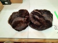 Two dark brown men's mink fur hats side by side on a white surface, showing the fur texture and ribbon detail.