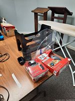 Unopened Microsoft wireless mice in retail packaging alongside clear plastic file organizer, black pencil holder, black tape dispenser, wooden side tables, and ironing board.