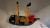 Side view of the Playmobil plastic pirate ship showing yellow rigging, pirate flag, and red deck area.
