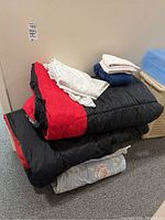 Three sleeping bags stacked with linens on top, showing the red and black flannel lined sleeping bags, hand towels, sheet, and pillowcase.