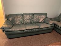 Front view of worn dark green leather three-seat sofa showing creased cushions and armrests.