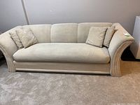 Full front view of beige fabric 3-seat sofa on carpet with two matching throw pillows.