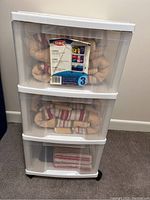Front view of white plastic 3-drawer storage unit with contents inside drawers, showing clear drawer fronts and white frame with label.