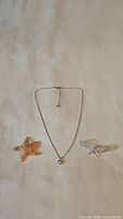 Full lot showing silver-tone crystal pendant necklace, gold-tone starfish brooch, and silver-tone starfish brooch.