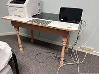 Overall side view of the work table with turned wood legs and black laminate top, showing chip damage on edges.