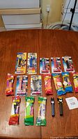 Full view of 17 PEZ dispensers laid out on table showing mostly packaged superhero dispensers and two loose dispensers