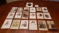 Photo showing full layout of 19 antique photographs on wooden table, mostly sepia tones, various framed mounts typical of late 1800s to early 1900s studio portraits.