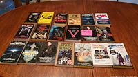 Photo shows 19 vintage paperback sci-fi and horror movie tie-in books arranged on a wooden table. Titles include The Fog, Star Wars, E.T., Jaws, The Exorcist, and others.