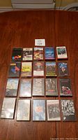 Photo showing all 20 cassette tapes arranged in rows on a wooden surface, title cards visible on tape covers.