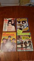 Five Beatles magazines arranged on wooden table, showing covers with John Lennon, Yoko Ono, and The Beatles images from 1970s and 1980s.