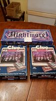 Photo of two Clue VCR Mystery Games and one Nightmare The Video Board Game in original boxes on a wooden table.